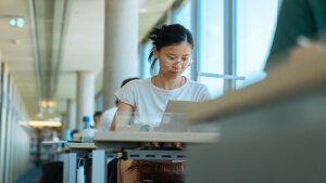 Person sitzt am Tisch und schaut auf den Laptop.