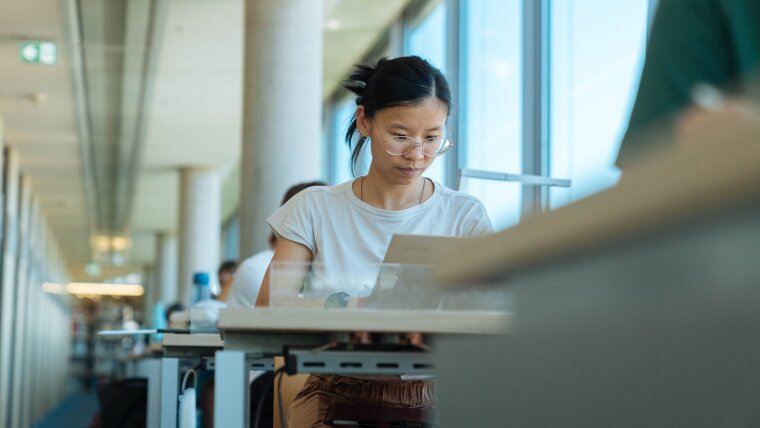 Person sitzt am Tisch und schaut auf den Laptop.
