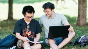 Zwei Personen sitzen auf einer Wiese und schauen auf einen Laptop.